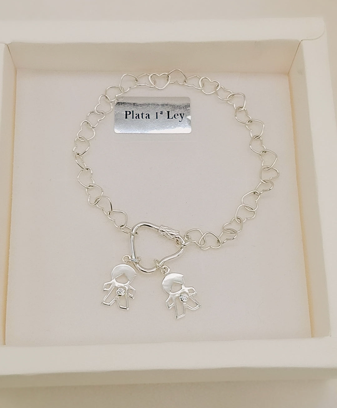 Pulsera de plata de ley 925 con cadena de corazones y dos charms de niño con circonitas brillantes, presentada en caja de regalo Pétalos de Plata.