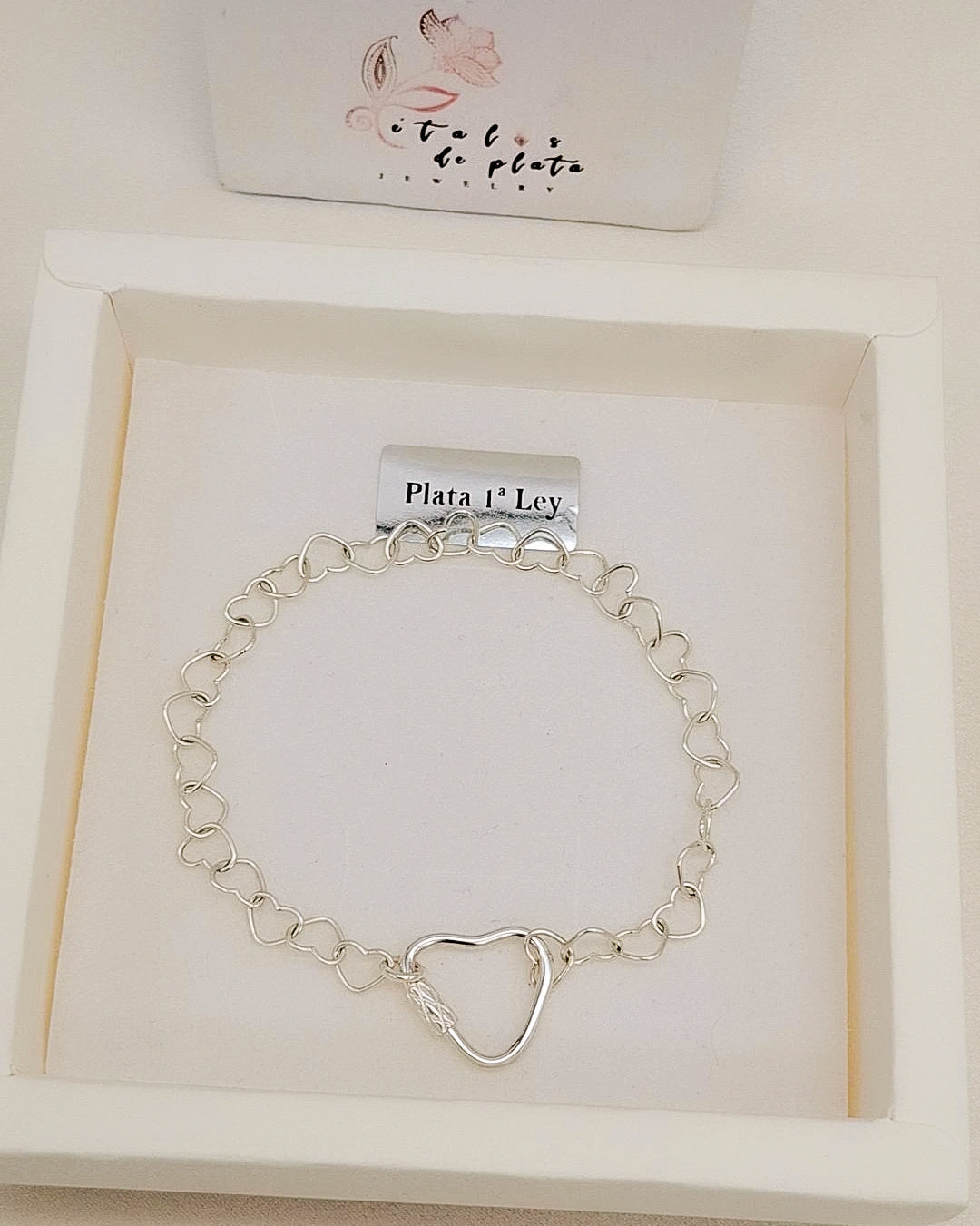 Pulsera de plata con eslabones en forma de corazón y cierre de corazón, presentada en caja blanca de joyería.