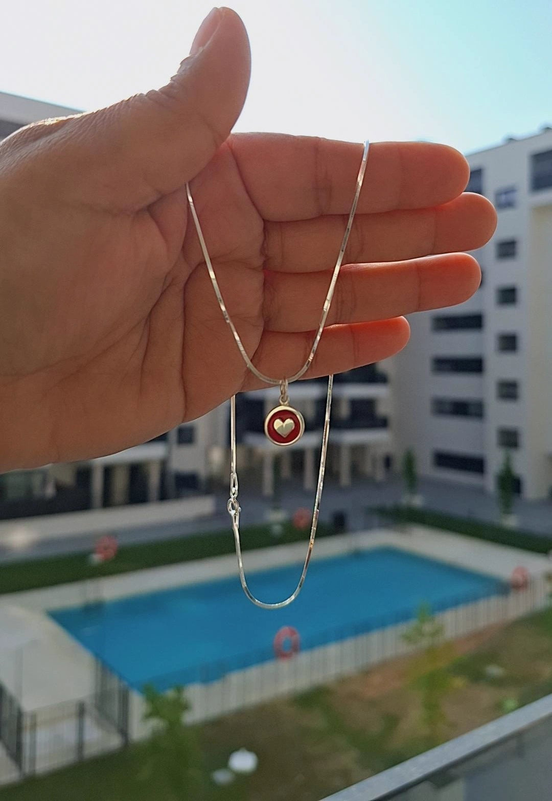 Collar artesanal elaborado en plata de ley 925, con un colgante circular esmaltado en rojo y un delicado corazón en relieve plateado en el centro.