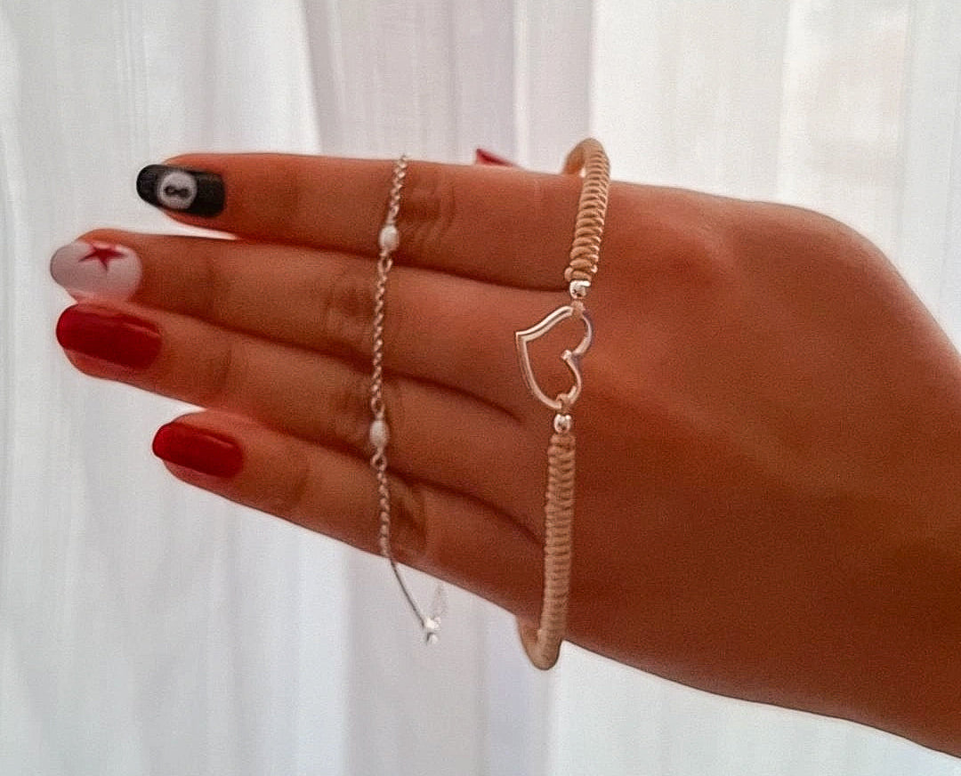Layering de pulseras delicadas con corazón y perlas